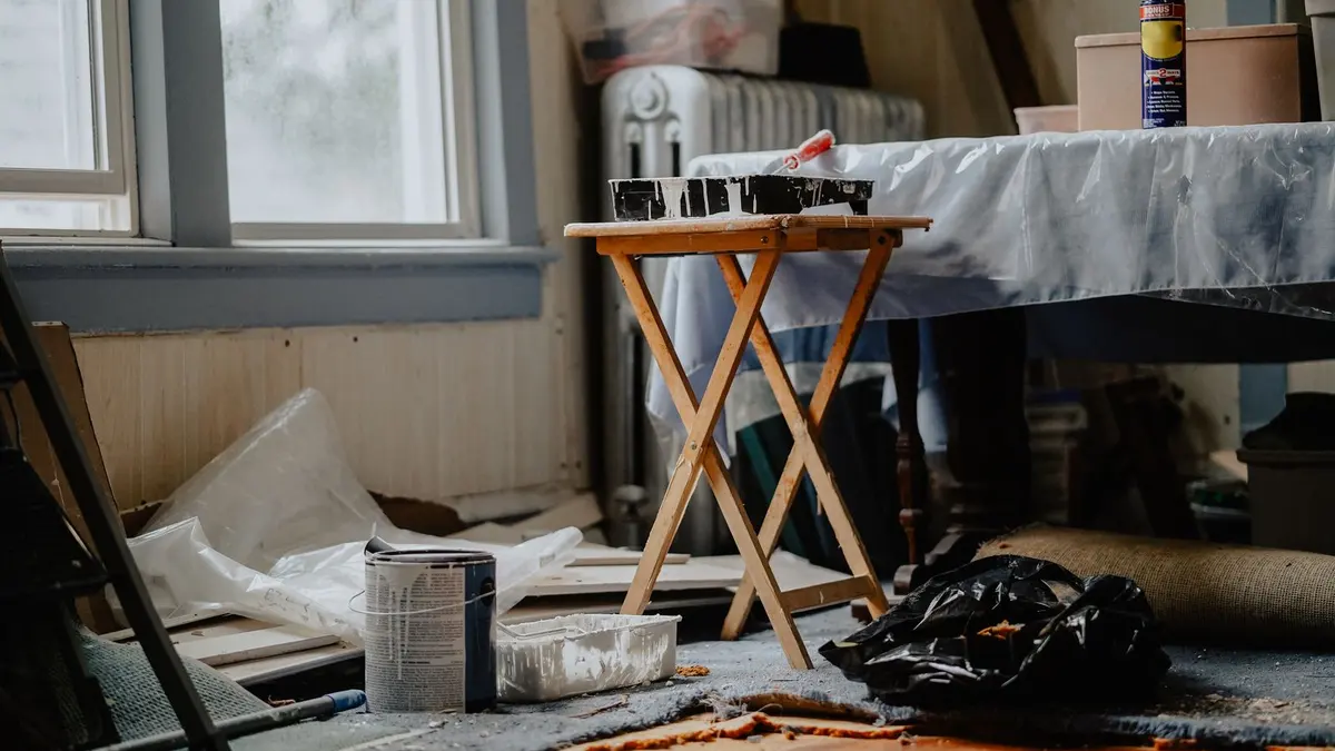 Un meuble en bois ancien posé sur une bâche, avec pinceau, papier abrasif et chiffon de nettoyage